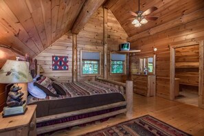 A log cabin bedroom with a bed, a lamp, a quilt, a window, and a ceiling fan. - Peaceful 3BR*MTN Views*Hot Tub*Pool Table*Fire Pit (Sevierville)