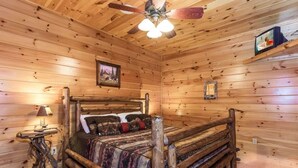 A wooden cabin interior with a bed, a ceiling fan, a lamp, and a framed picture on the wall. - Peaceful 3BR*MTN Views*Hot Tub*Pool Table*Fire Pit (Sevierville)