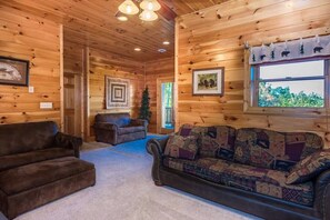 Ein gemütliches Blockhaus-Interieur mit einem braunen Ledersofa, einem gemusterten Couchsofa und einer Holzbalkendecke.