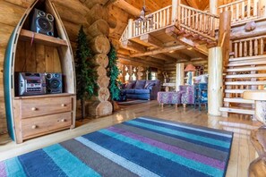 A log cabin interior with a wooden staircase, a sofa, a coffee table, and a decorative log wall. - Peaceful 3BR*MTN Views*Hot Tub*Pool Table*Fire Pit (Sevierville)