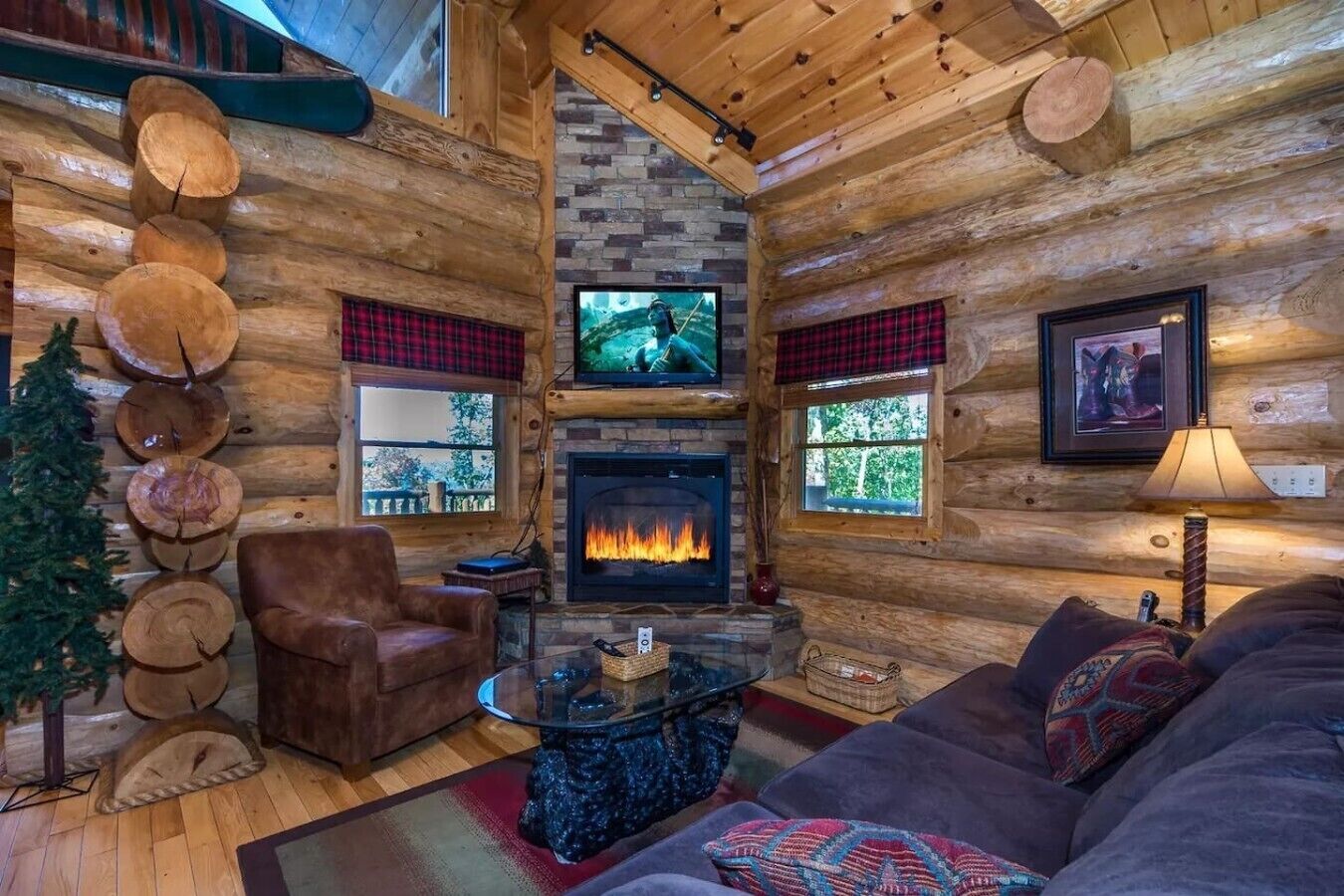 A log cabin interior with a fireplace, a television, a couch, and a coffee table.