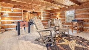 Ein rustikales Holzhäuschen im Inneren mit Holzboden, einem Teppich mit Sternenmuster, einem Kicker, einem Schreibtisch mit Computer und einem Stuhl.