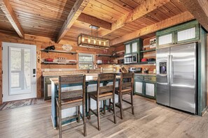 Eine rustikale Küche mit Holzbalken, einem Edelstahlkühlschrank und einer Bar mit Holzstühlen.