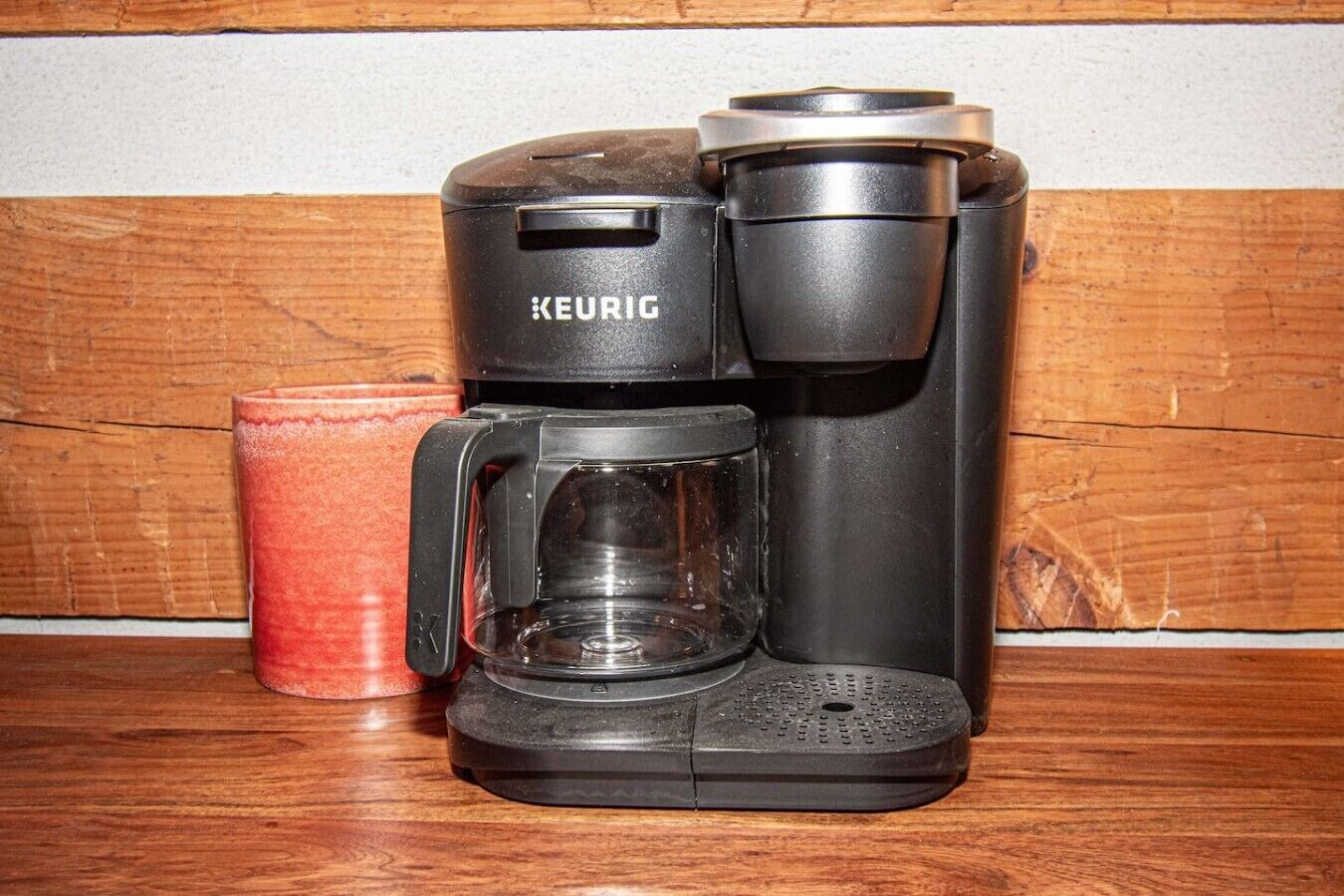 A Keurig coffee maker with a glass carafe and a red mug on a wooden surface.