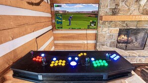 Ein Holzinnenraum mit einem Fernseher, der ein Golfspiel zeigt, einem Kamin und einem Billardtisch mit beleuchteten Knöpfen.