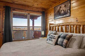 Une chambre rustique en bois, avec un lit, une grande fenêtre et une image d’ours accrochée au mur.
