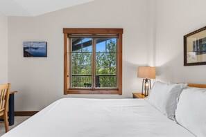 Ein Schlafzimmer mit einem großen Bett, einem Fenster mit Blick ins Grüne, einem Nachttisch mit Lampe und einem Sessel.
