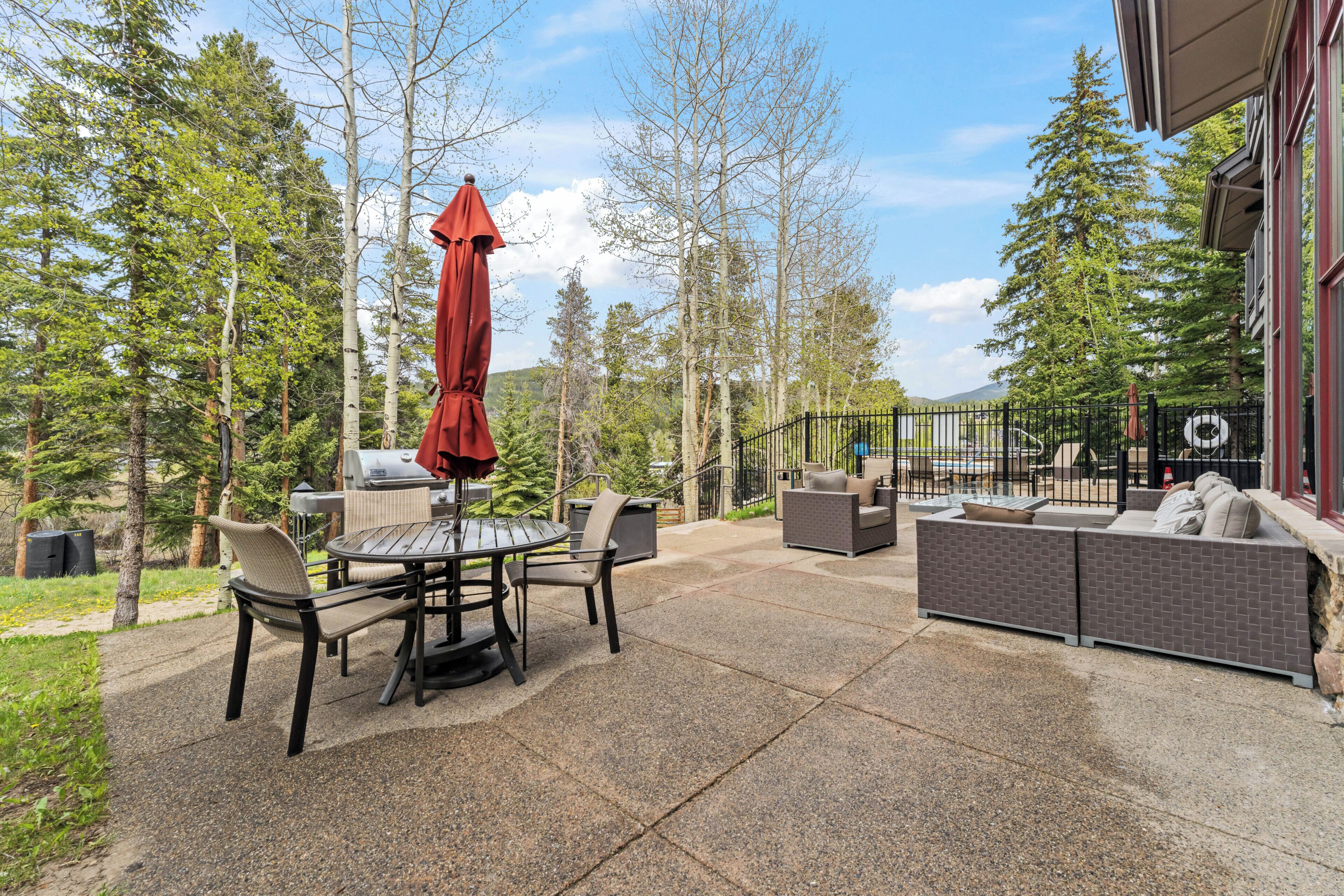 An outdoor patio with a table and chairs, a red umbrella, and a sofa.