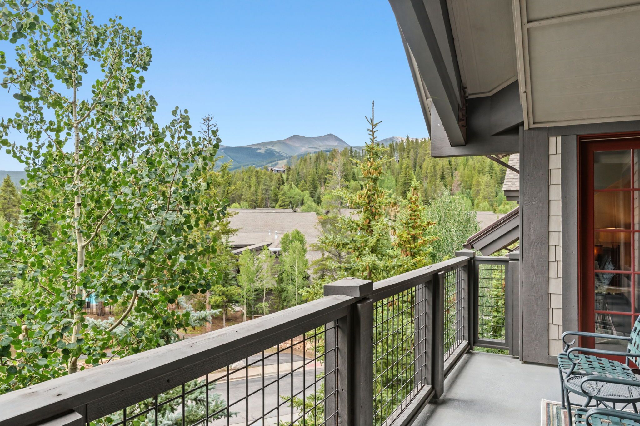 A balcony with a view of mountains, trees, and a building in the distance.