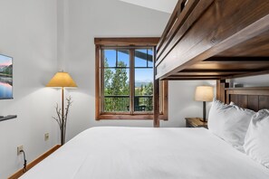 A bedroom with a large bed, a window with a view of greenery, and a wooden ceiling. - Beautiful Three-Bedroom Penthouse in Mountain Thunder Lodge (Breckenridge)
