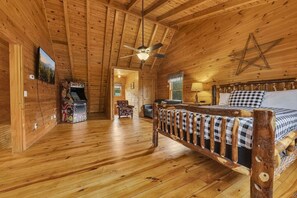 A wooden cabin interior with a bed, a ceiling fan, and a view of the outdoors. - Creekside 3BR w/Fire Pit and Hot Tub! Peaceful! (Cosby)