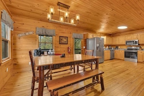 Ein Holzblockhaus-Interieur mit Esstisch, Bänken, einer Küche mit Geräten und einem Schild an der Wand.