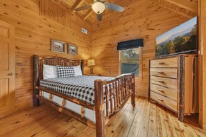 Ein Schlafzimmer einer Holzhütte mit Bett, Schminktisch und Deckenventilator.
