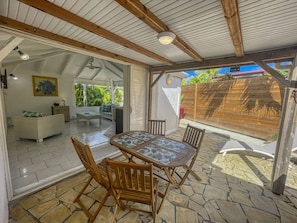 A covered patio with a stone floor, wooden furniture, and a view of a lush garden. - Charming villa with pool - 2 guests (Saint-François)