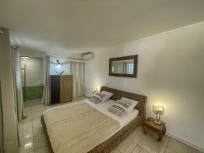 A bedroom with a bed, bedside lamps, a mirror, and a bathroom visible in the background. - Charming villa with pool - 2 guests (Saint-François)