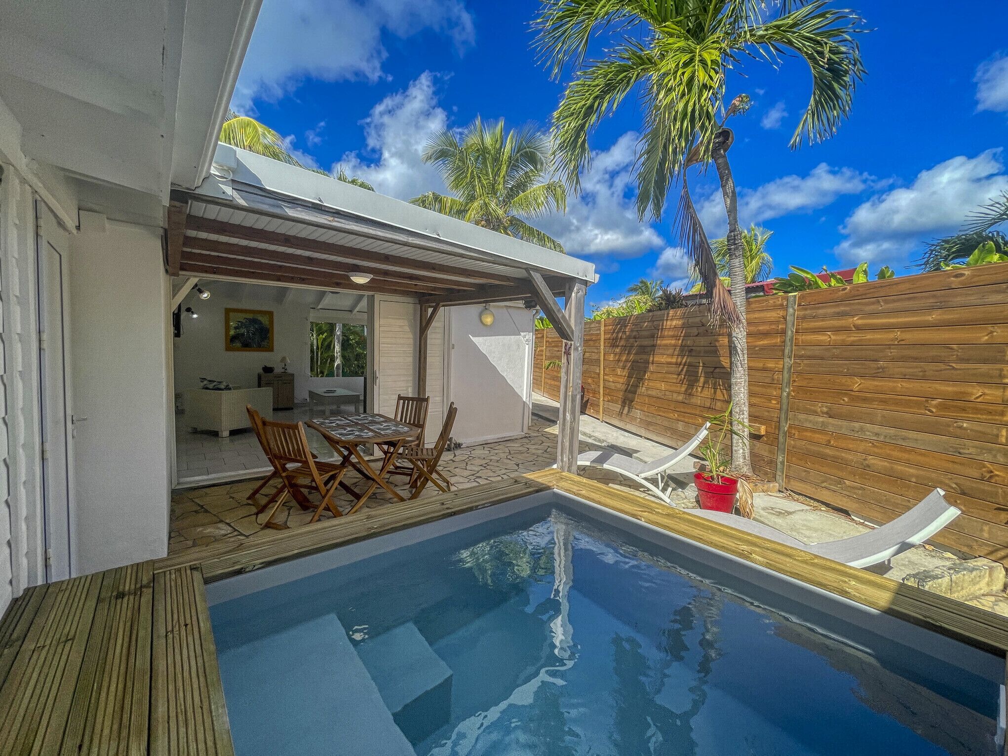 A pool area with a wooden deck, lounge chairs, and a covered seating area with a table and chairs.