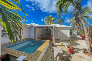 A pool area with a wooden deck, a covered seating area, and palm trees. - Charming villa with pool - 2 guests (Saint-François)