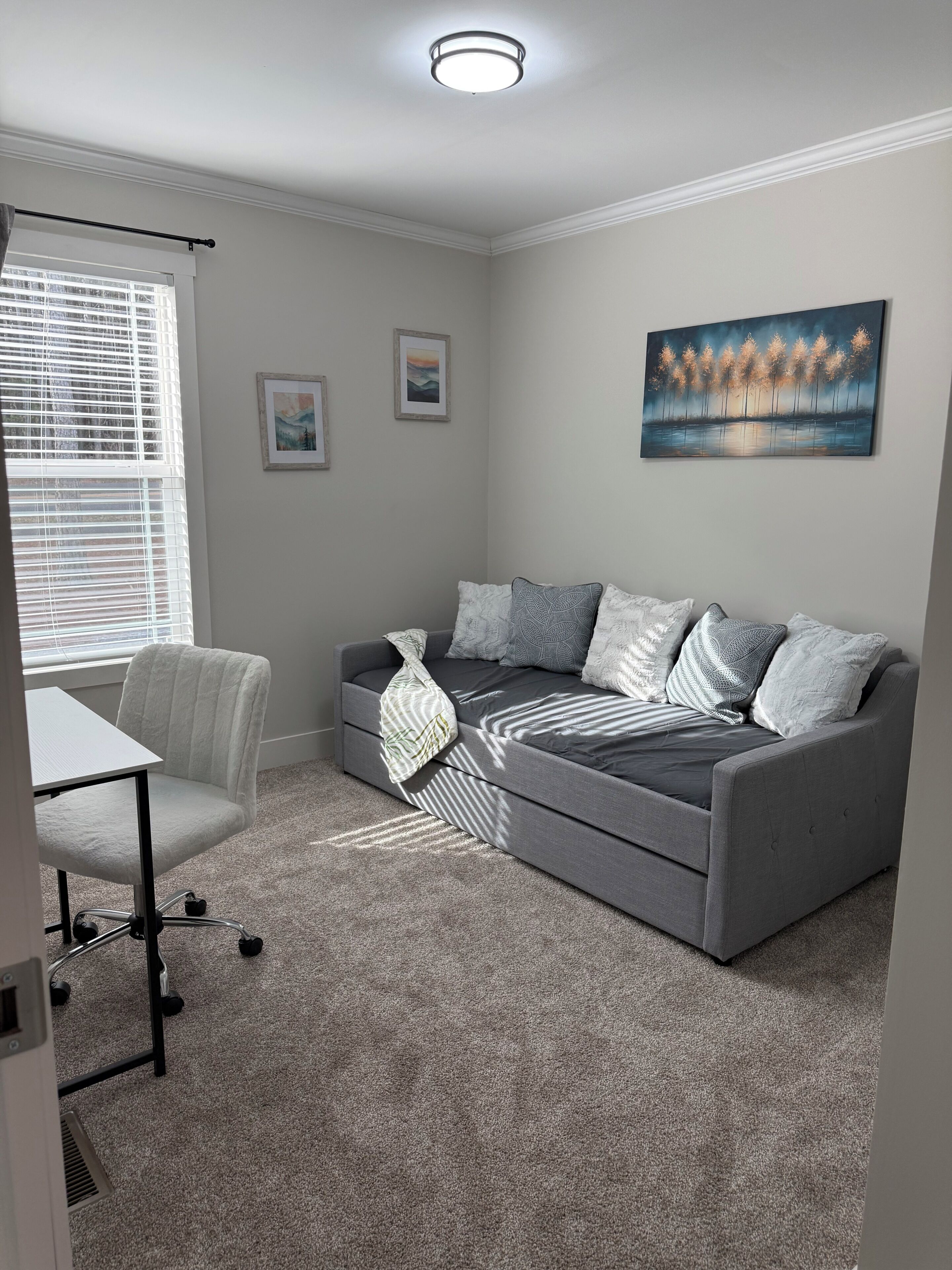 A modern living room with a grey sofa, white armchair, and a small table. There are framed pictures on the wall and a ceiling light.