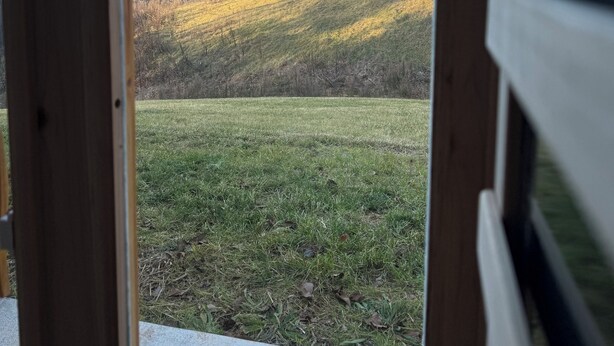 Une vue à travers une fenêtre à cadre en bois, donnant sur un champ verdoyant et des collines lointaines.