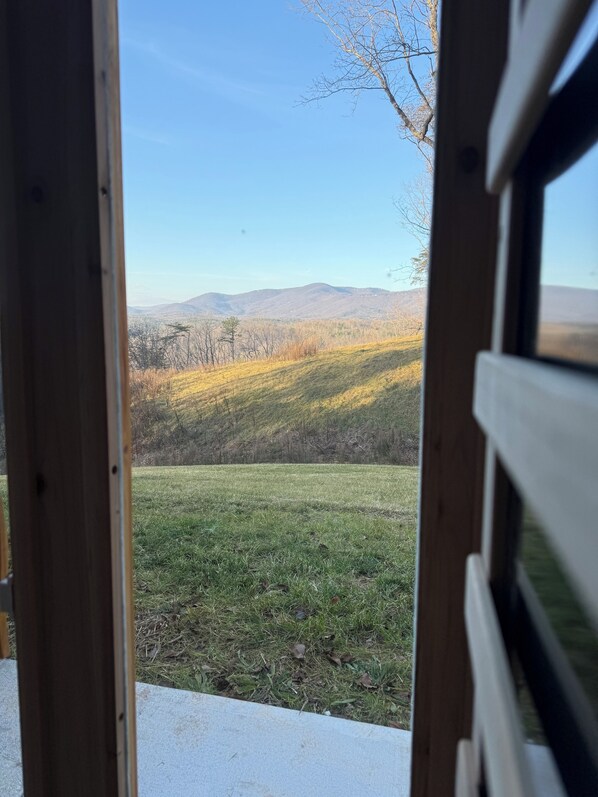 A view through a window with a wooden frame, overlooking a grassy field and distant hills.