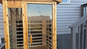 Une structure en bois dotée d’une porte et de fenêtres en verre, placée contre une maison dont les murs sont recouverts de bardage et qui possède une fenêtre au-dessus.