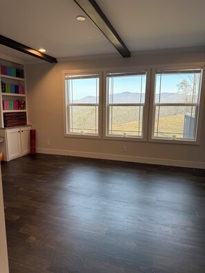 A spacious room with a large window, a built-in shelf with colorful storage, and a dark wooden floor.