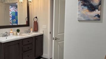 Un baño con tocador doble, muebles de madera oscura, alfombra estampada y un espejo grande con candelabro.