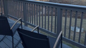 Une terrasse avec deux chaises et une rambarde en métal, d’où l’on peut admirer un paysage boisé avec des montagnes à l’horizon.