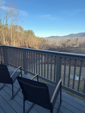 A deck with two chairs and a metal railing overlooking a forested landscape with mountains in the distance.