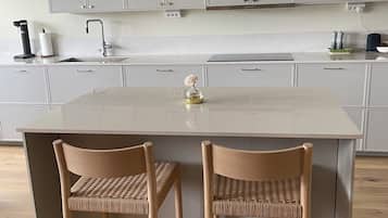 A modern kitchen with a central island, two wicker chairs, and a stainless steel sink.