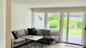 A modern living room with a sectional sofa, a coffee table, and a view through large sliding glass doors to a garden.