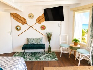 A room with a bed, a sofa, a TV mounted on the wall, a window with a view of the sea, and a chair with a plant. - Waterfront Paradise 4 bedroom Villa SXM (Koolbaai)
