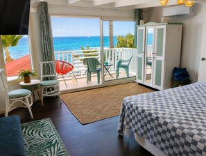 A room with a bed, a small table with chairs, a view of the ocean, and a balcony with a railing. - Waterfront Paradise 4 bedroom Villa SXM (Koolbaai)