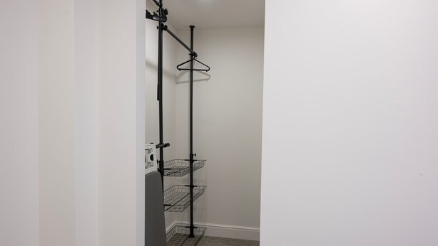 Ein Blick in den Raum zeigt eine schwarze Metallregalkonstruktion an einer weißen Wand, mit mehreren Regalböden und Haken.