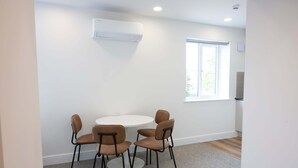 Ein Zimmer mit einem runden Tisch, vier Stühlen, einer Wand-Klimaanlage und einem Fenster mit Jalousien.