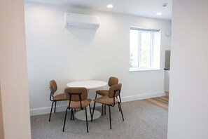 Ein Zimmer mit einem runden Tisch, vier Stühlen, einer Wand-Klimaanlage und einem Fenster mit Jalousien.