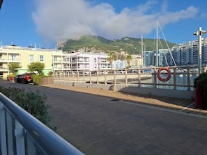 Un passeig marítim amb una vorera per a vianants, un salvavides i vista d'una marina amb vaixells i edificis al fons.