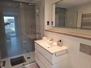 Ein modernes Badezimmer mit Duschabtrennung aus Glas, einem weißen Waschtisch mit Spiegel und einem Handtuchhalter.