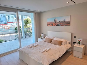 A modern bedroom with a large bed, a nightstand, a bedside table, and a painting on the wall.