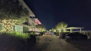 A nighttime street view with a paved walkway, a parked car, and buildings with illuminated windows. - Luxury Marina Resort | Rock Views & Pools - Apartment (Gibraltar)