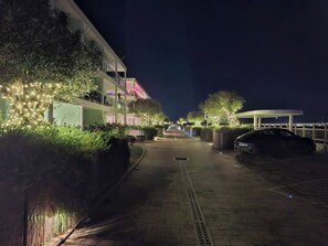 A nighttime street view with a paved walkway, a parked car, and buildings with illuminated windows. - Luxury Marina Resort | Rock Views & Pools - Apartment (Gibraltar)