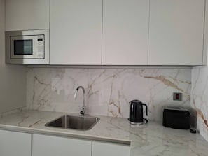 A kitchen with a stainless steel sink, a microwave, a kettle, and a toaster.