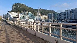 A waterfront promenade with a white fence, a cruise ship docked on the left, and buildings in the background. - Luxury Marina Resort | Rock Views & Pools - Apartment (Gibraltar)
