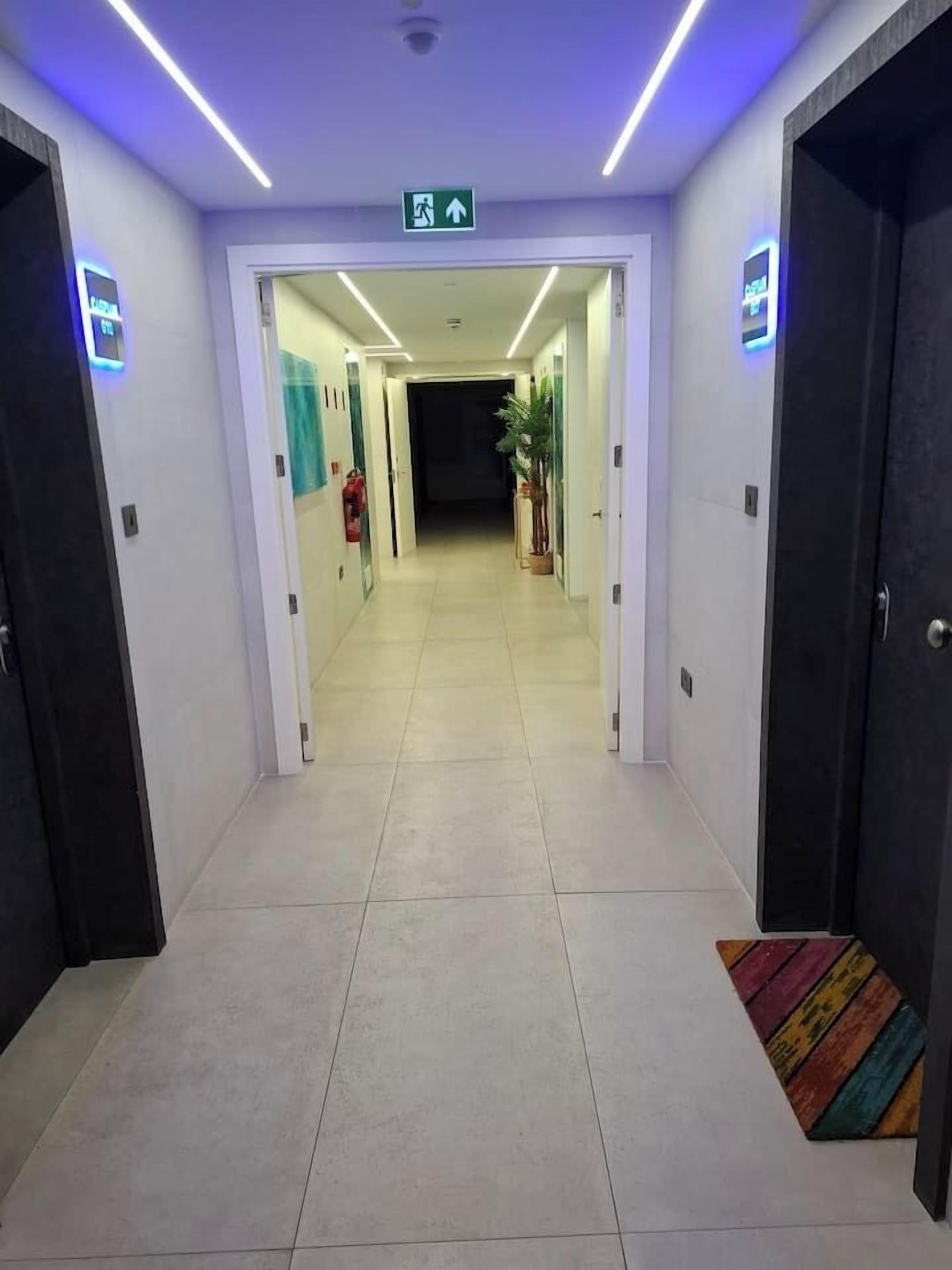 Un pasillo de hotel con puertas a ambos lados, un cartel de indicaciones en el techo y piso de baldosas.