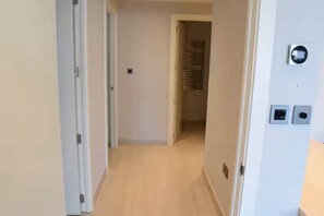 A hallway with a door on the left, a light switch, and a thermostat on the right.
