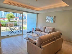 A modern living room with a sofa, a coffee table, and a dining area with chairs. - Luxury Marina Resort | Rock Views & Pools - Apartment (Gibraltar)