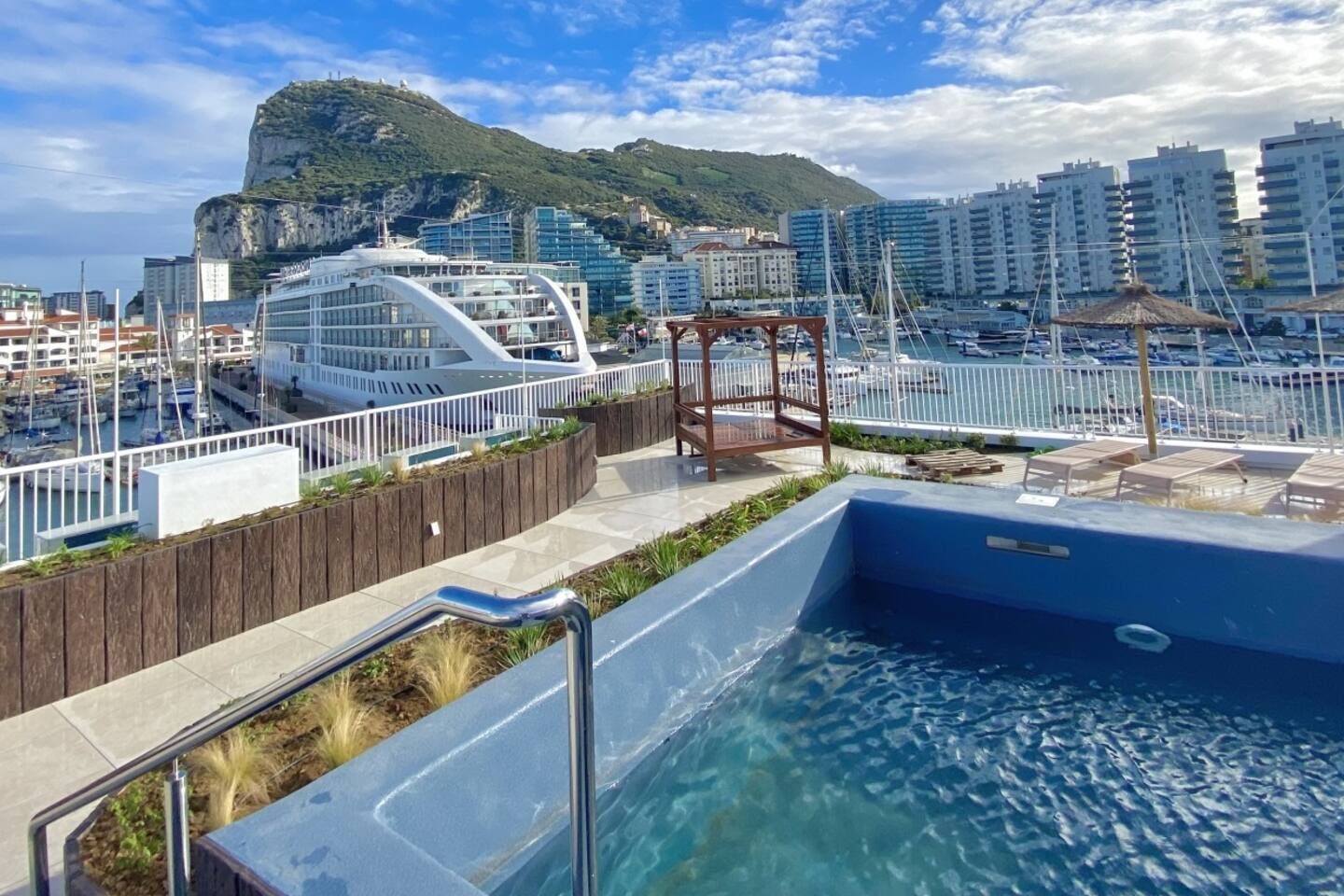 A swimming pool with a wooden deck and a view of a cityscape with buildings and a mountain in the background.