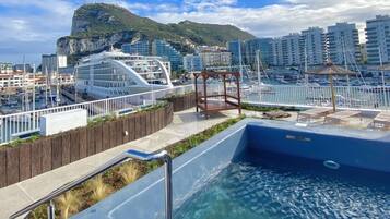 A swimming pool with a wooden deck and a view of a cityscape with buildings and a mountain in the background.
