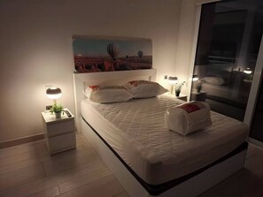 Un dormitori modern amb un llit, taules de nit i un quadre a la paret.