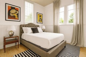 Quarto com uma cama grande, duas mesas de cabeceira com luminárias, um tapete listrado e dois quadros na parede.